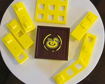 Könnte beinhalten: Ein Satz gelber Plastik-Puzzleteile mit einer braunen Holzbasis. Die Puzzleteile haben verschiedene Formen und Größen. Die Holzbasis hat ein Entenlogo darauf.