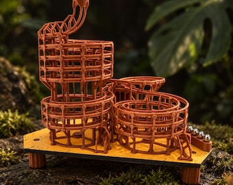 May include: A brown 3D-printed marble run toy featuring a tall spiral track structure mounted on a yellow hexagonal base. The intricate lattice design includes multiple levels and curves, with a small row of silver metal marbles resting on the side.