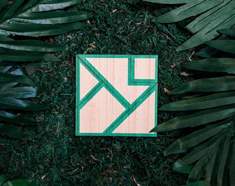 Könnte beinhalten: Ein hölzernes Tangram-Puzzle mit hellem Holzmaserungsfinish und grün lackierten Kanten. Das Puzzle besteht aus geometrischen Formen und ist vor einem Hintergrund aus grünem Moos und dunkelgrünen Blättern platziert. Ein klassischer Denksport.