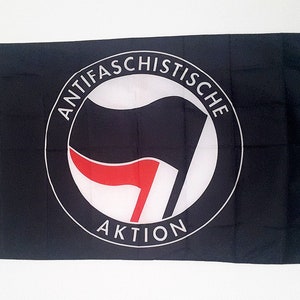 Puede incluir: Una bandera negra con un círculo blanco que contiene un puño estilizado rojo y negro y el texto "ANTIFASCHISTISCHE AKTION".