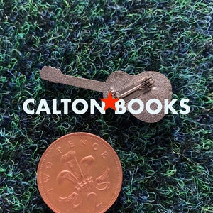 May include: A silver guitar pin with the text "CALTON BOOKS" in white letters. The pin is on a green surface with a copper British penny coin.