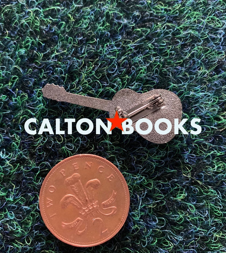 May include: A silver guitar pin with the text "CALTON BOOKS" in white letters. The pin is on a green surface with a copper British penny coin.