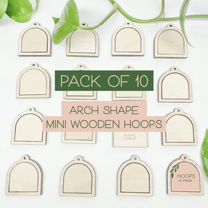 May include: A pack of 10 mini wooden hoops in an arch shape. The hoops are unfinished and ready to be decorated. The text "PACK OF 10" and "ARCH SHAPE MINI WOODEN HOOPS" is printed on the image. The image also includes a small square with the text "HOOPS n' more" printed on it.