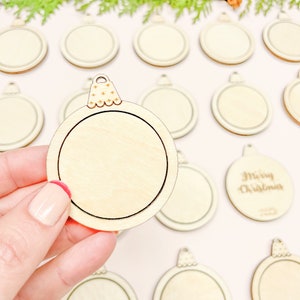 May include: A set of unfinished wooden Christmas ornament shapes. The ornaments are round and have a small loop at the top. One ornament has the words "Merry Christmas" engraved on it.