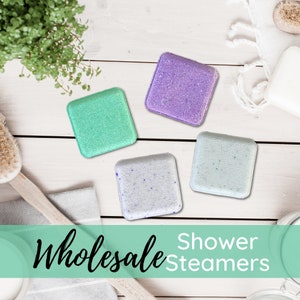 May include: Four square shower steamers in different colors: green, purple, white with blue flecks, and light blue. The text "Wholesale Shower Steamers" is on a green background.