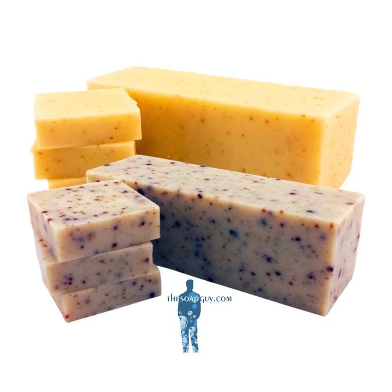 May include: A stack of four bars of handmade soap with a speckled appearance. The soap bars are arranged in a pyramid shape. The top bar is a light beige color, while the bottom three bars are a light gray color with dark speckles. The soap bars are arranged on a white surface.