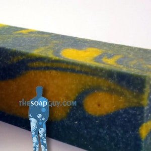 May include: A large bar of handmade soap with a blue and yellow swirl pattern. The soap is textured and has a speckled appearance. The text "thesoapguy.com" is visible on the soap.