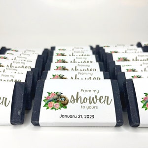 May include: A collection of black soap bars with white labels. The labels feature a floral design with birds and a nest. The text on the labels reads "From my shower to yours" and "January 21, 2023".