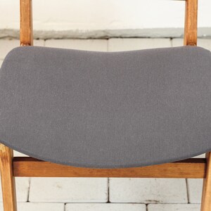 K&ouml;nnte beinhalten: Ein grauer Polsterstuhl mit einem Holzrahmen. Der Stuhl hat eine geschwungene Sitzfl&auml;che und ein schlichtes Design.