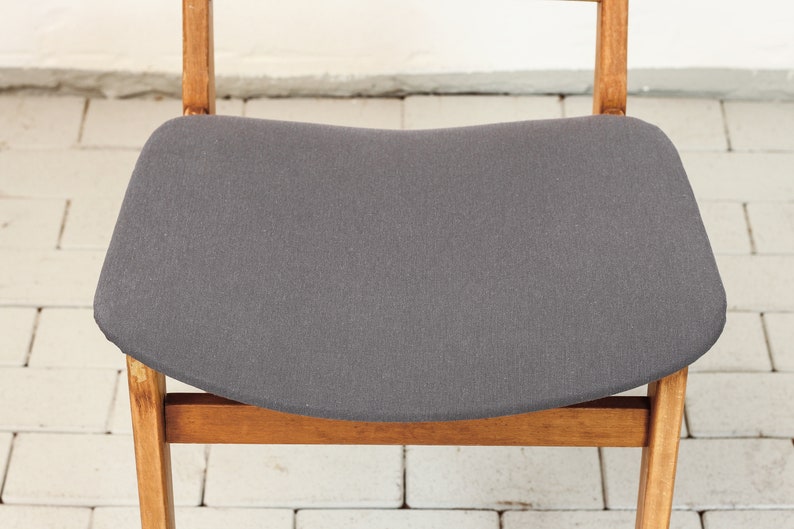 K&ouml;nnte beinhalten: Ein grauer Polsterstuhl mit einem Holzrahmen. Der Stuhl hat eine geschwungene Sitzfl&auml;che und ein schlichtes Design.