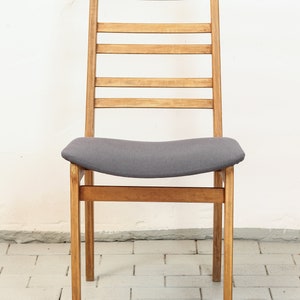 K&ouml;nnte beinhalten: Ein Holzstuhl mit einem grauen Stoffbezug. Der Stuhl hat eine Leiter-R&uuml;ckenlehne mit horizontalen Leisten.