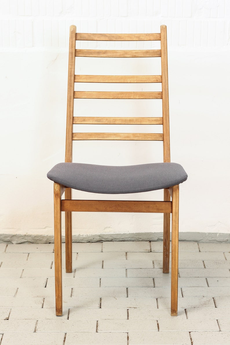 K&ouml;nnte beinhalten: Ein Holzstuhl mit einem grauen Stoffbezug. Der Stuhl hat eine Leiter-R&uuml;ckenlehne mit horizontalen Leisten.