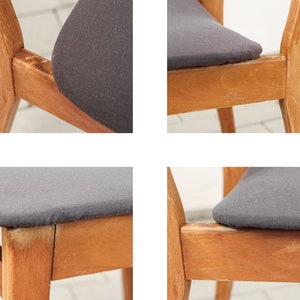 K&ouml;nnte beinhalten: Nahaufnahme eines Holzstuhls mit einem dunkelgrauen Stoffbezug. Der Stuhl hat ein schlichtes Design mit einer leicht geschwungenen R&uuml;ckenlehne und geraden Beinen. Der Stoffbezug ist glatt und wirkt abgenutzt.