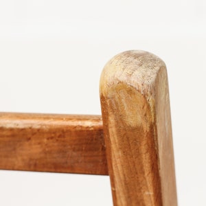 K&ouml;nnte beinhalten: Nahaufnahme eines Stuhlbeins aus Holz mit einer abgenutzten, hellbraunen Oberfl&auml;che. Die Holzmaserung ist sichtbar und das Bein hat eine abgerundete Oberseite.
