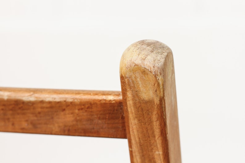 K&ouml;nnte beinhalten: Nahaufnahme eines Stuhlbeins aus Holz mit einer abgenutzten, hellbraunen Oberfl&auml;che. Die Holzmaserung ist sichtbar und das Bein hat eine abgerundete Oberseite.