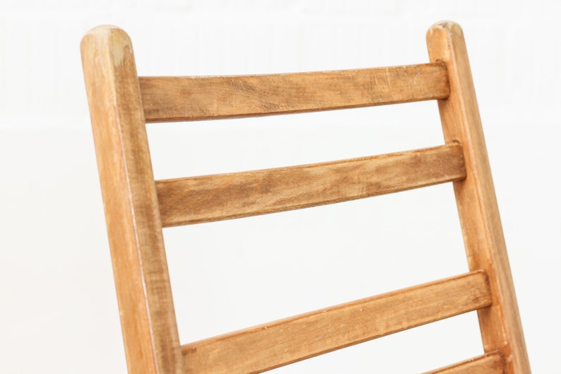 K&ouml;nnte beinhalten: Nahaufnahme der R&uuml;ckenlehne eines Holzstuhls mit einer Leiter-R&uuml;ckenlehne. Der Stuhl ist aus hellbraunem Holz gefertigt und hat eine nat&uuml;rliche Oberfl&auml;che.