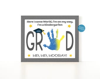 May include: A framed print with the words "GRAD" and a handprint in blue and yellow. The text "Here I come World, I'm on my way, I'm a Kindergarten" and "HIP, HIP, HOORAY!" are also included. A graduation cap and the year 2026 are also featured.
