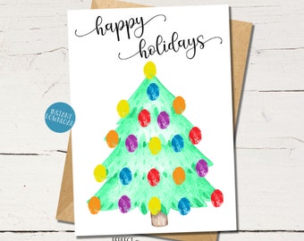 Può includere: Un biglietto di Natale stampabile con un'illustrazione ad acquerello di un albero di Natale verde con ornamenti colorati. Il testo "happy holidays" è scritto in corsivo nella parte superiore del biglietto.