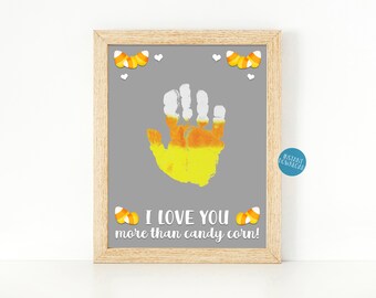 Puede incluir: Un diseño de arte de huella de mano imprimible con una huella de mano de maíz de caramelo amarillo y naranja y el texto "¡Te quiero más que al maíz de caramelo!"