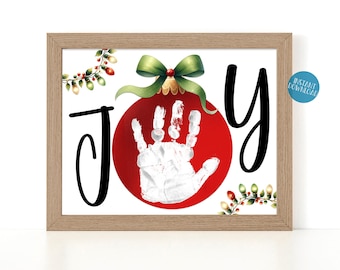 May include: A printable Christmas ornament with a red background and a white handprint inside. The ornament is surrounded by green and red holly and the word "JOY" is written in black cursive.