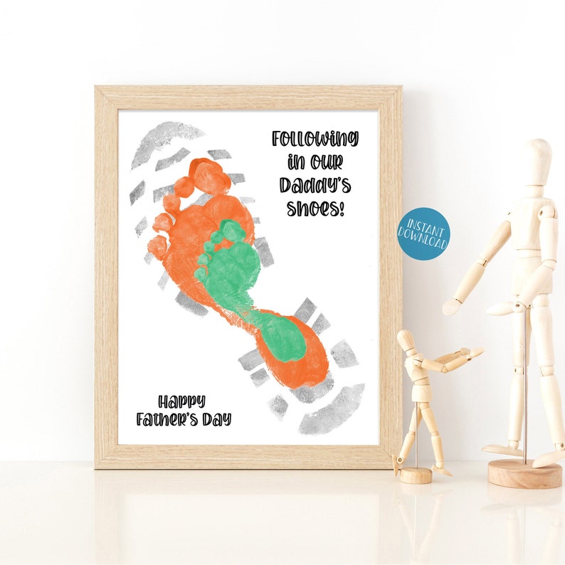 May include: A printable Father's Day card with a footprint design. The footprint is made with orange and green paint and is set against a gray background. The text reads "Following in our Daddy's shoes!" and "Happy Father's Day".