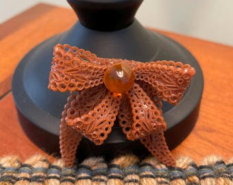 Vintage celluloid brooch pin featuring an amber colored bow design with intricate filigree cut-out details