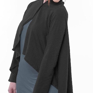 May include: A black, textured, open-front cardigan with long sleeves. The cardigan has a draped, asymmetrical design. The model is wearing a gray top and pants. The cardigan is made of a soft, flowing fabric.