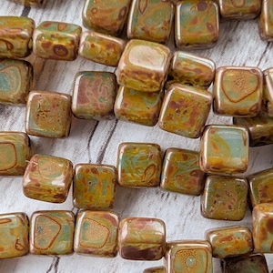 May include: Close-up of square beads in shades of brown, green, and gold. The beads have a mottled, textured appearance, and are strung together. These beads are suitable for jewelry making and other craft projects.