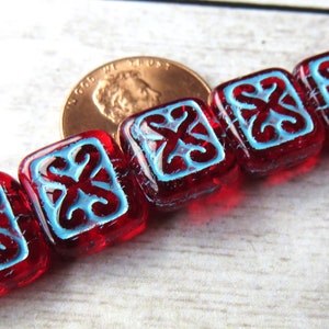 May include: A strand of red glass beads with a blue swirl design. The beads are square shaped and have a glossy finish.