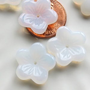May include: Five white opal flower-shaped beads with a hole in the center. The beads are arranged on a white surface with a penny for scale.