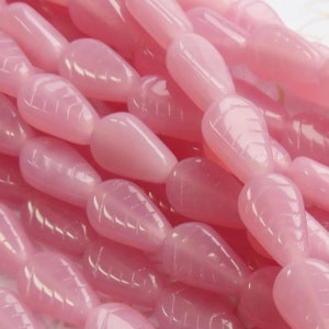 May include: A strand of pink, teardrop-shaped beads with a carved leaf design. The beads are made of glass or gemstone and have a smooth, polished finish.