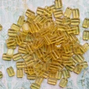 May include: A large pile of translucent yellow glass beads, each bead is rectangular with a flat top and bottom. The beads are arranged in a random pattern.