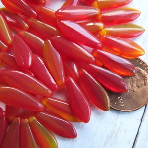 May include: A pile of red and orange glass beads, some with a yellow tint, arranged in a fan shape. A US penny is included for scale.