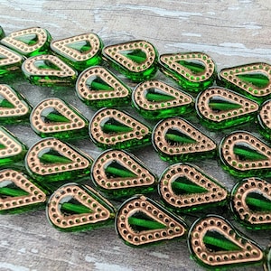 May include: Close-up of green teardrop-shaped beads with a copper-colored border. The beads have a glossy finish and are arranged in rows. The copper border is dotted with small holes. These beads are suitable for jewelry making.