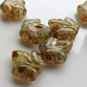 May include: Five glass beads in the shape of leaves with gold accents and brown and white swirls.
