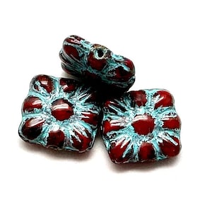 May include: Three square-shaped ceramic beads with a red and turquoise glaze. The beads have a raised flower design.