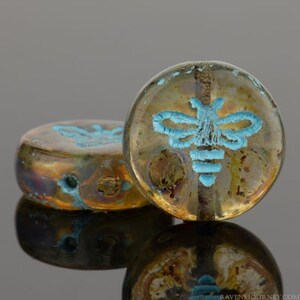 May include: Two round glass beads with a metallic gold and brown iridescent finish. The beads have a blue bee design on them.