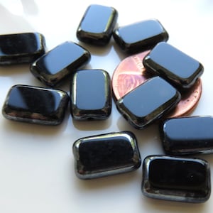May include: A group of 12 black rectangular glass beads with a shiny finish. The beads are scattered on a white surface with a copper penny in the center.