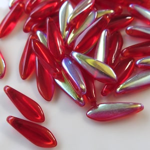 May include: A pile of red and iridescent glass beads in a teardrop shape. The beads have a shiny, reflective finish.