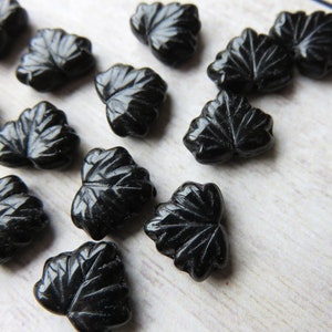 May include: A collection of black glass leaf-shaped beads. The beads are all the same size and shape, and they have a glossy finish.