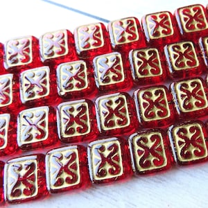 May include: Red glass square beads with a gold metallic design. The beads have a slightly textured surface.