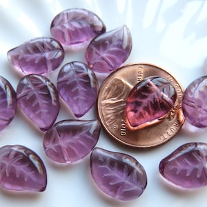 May include: A group of 15 purple glass leaf beads with a raised vein pattern. The beads are approximately the size of a US penny.