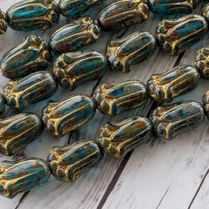 May include: Close-up of a strand of artisan beads. The beads are a mix of teal, brown, and gold. Each bead has a unique shape with gold accents. The beads are strung on a white string, ready for jewelry making.