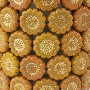 May include: Close-up of a string of orange glass beads with a gold-toned daisy design. The beads are arranged in a circular pattern.