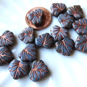 May include: A collection of gray glass leaf-shaped beads with copper accents. The beads are scattered on a white surface.