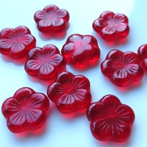 May include: Ten red glass flower-shaped embellishments with a raised design.