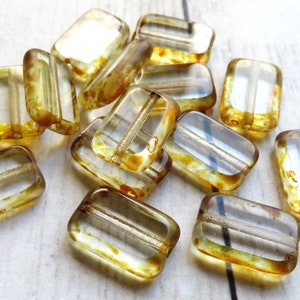 May include: A group of clear glass beads with a brown, speckled pattern. The beads are rectangular in shape and have a hole running through the center.