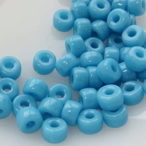 May include: A pile of light blue glass beads with a hole in the center of each bead. The beads are round and have a smooth, glossy finish.