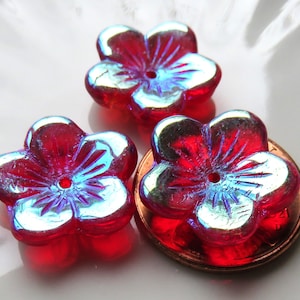 May include: Three red iridescent glass flower beads with a blue iridescent sheen. The beads are in the shape of a five-petal flower with a hole in the center.