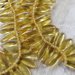 May include: A strand of translucent yellow glass beads in a leaf shape. The beads are strung together with a thin white thread.